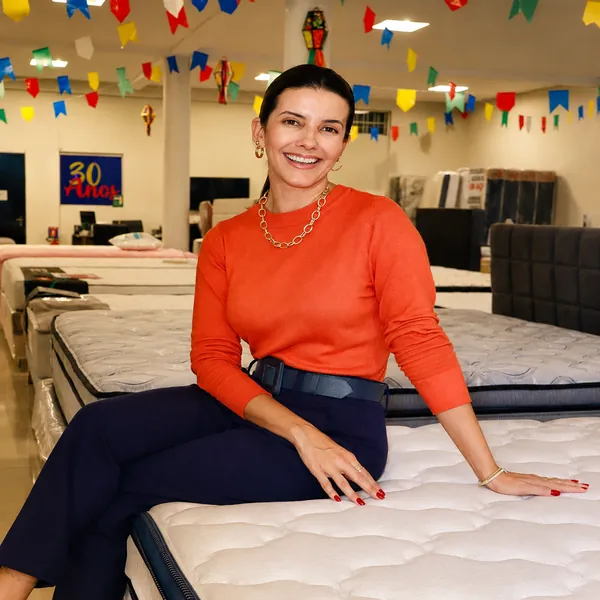 Atendente da Casa dos Colchões sentada em uma cama box no salão decorado com bandeirinhas juninas