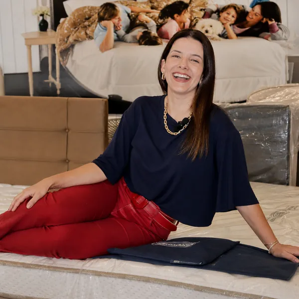 Atendente da Casa dos Colchões apoiada em um colchão do showroom