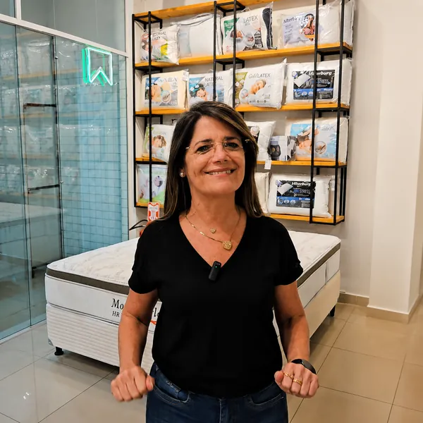 Atendente da Casa dos Colchões em frente à prateleira de travesseiros da loja