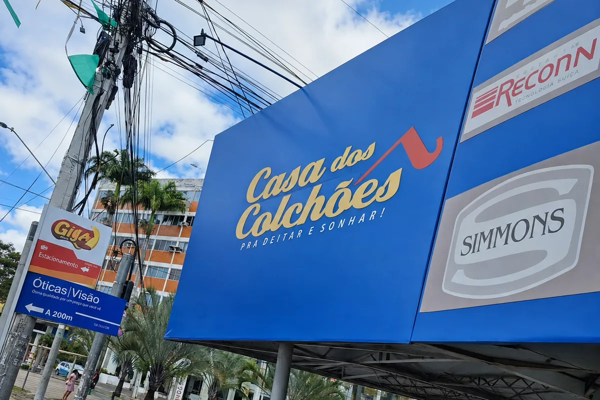 Painel azul da Casa dos Colchões com o slogan pra deitar e sonhar, instalado em avenida movimentada de Caruaru